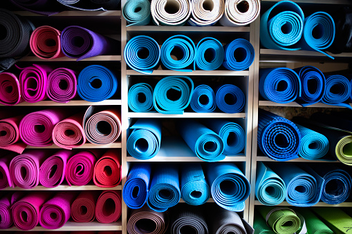 Blue and pink exercise mats lying rolled up on shelves in gym repository