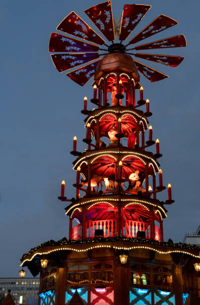 Blue and red night Christmas lights of traditional wooden carousel with catholic nativity scenes in Berlin Germany. Fairy tale lighted Christmas pyramid. Retro tower at Christmas fair in Europe stock photo