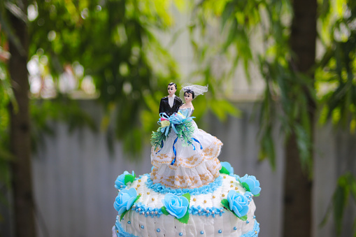 Blue and white wedding cake with wedding couple statue and blurred background at an outdoor wedding concept