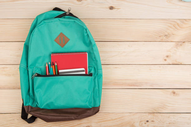 blue backpack, red notebooks and pencils on wooden table stock photo