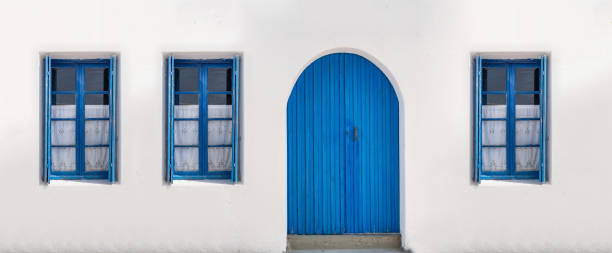 Blue door and three windows with open shutters on white wall. Greek island house front view stock photo