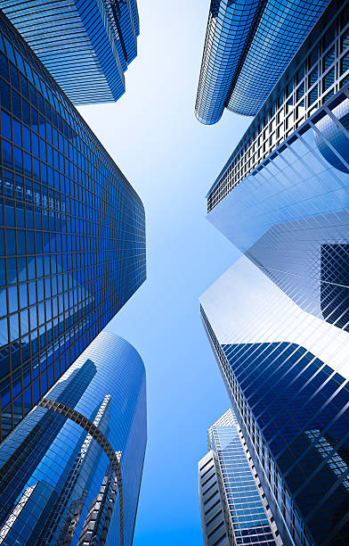 blue highrise glass skyscraper street low angle shot street of highrise glass skyscraper buildings low angle shot in blue dominant against a clear sky directly below stock pictures, royalty-free photos & images