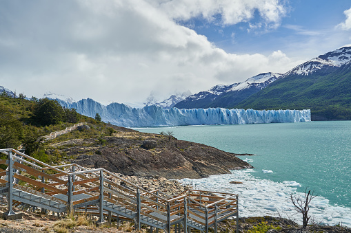 Blue ice of Perito Moreno Glacier in Glaciers national park in Patagonia, Argentina with the turquoise water of Lago Argentino in the foreground, dark green forests and sow covered mountains of the Andes in the distance_6