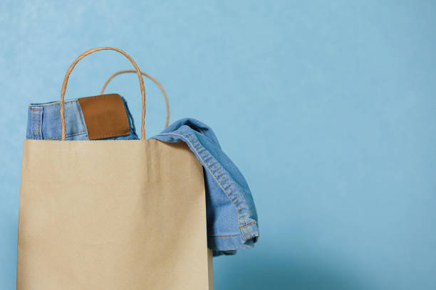 Blue jeans in a paper craft bag on a blue background. Concept of thrift stores, resale, second hand. Copy space. Blue jeans in a paper craft bag on a blue background. Concept of thrift stores, resale, second hand. Copy space. thrift store stock pictures, royalty-free photos & images