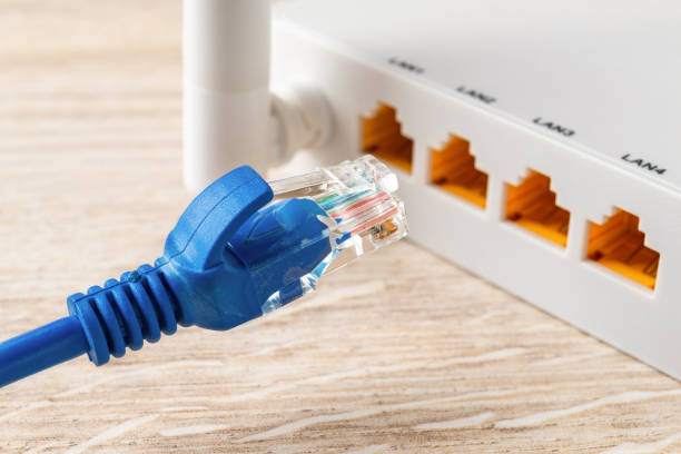 Blue network cable plug almost inserted into the yellow socket of white wi-fi wireless router. Wlan router for home and office for internet connection. Internet hardware concept. stock photo