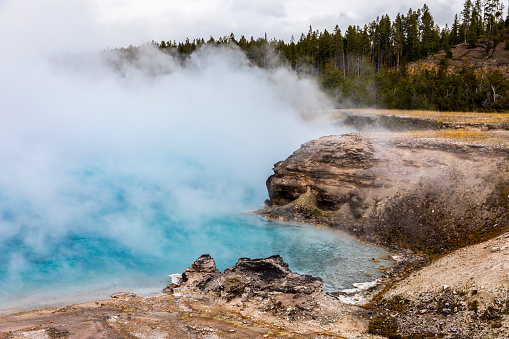 Natural scene of boiling blue pond geyser basin with white smoke inside dangerous hot zone in Yellowstone national park, Wyoming, USA.