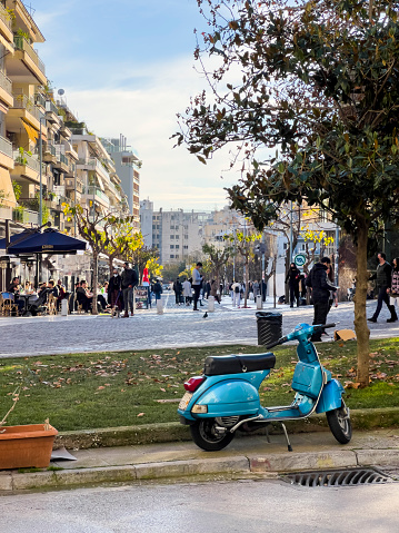 Athens, Greece - January, 1st 2022:  People walking around Acropolis Square, the museum neighborhood in the old town of Athens. Photo contains many locals and tourists visiting the square. Street coffee with sitting civilians. A cute blue motor vehicle is parking.