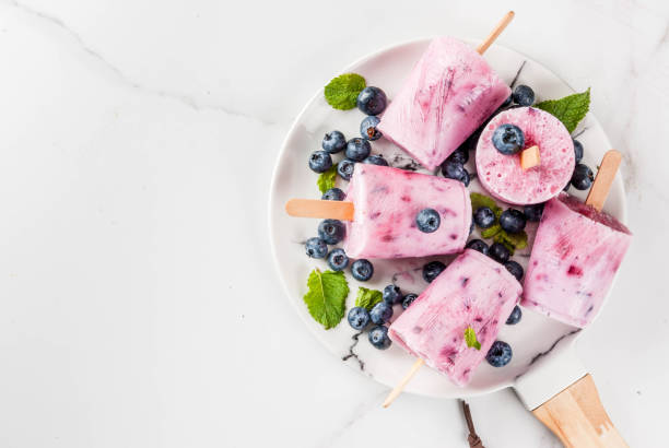 Blueberry ice cream popsicles Summer sweets and desserts. Vegan food. Frozen drinks, smoothies. Ice cream popsicles from homemade Greek yogurt and fresh organic blueberries. With mint. On plate, white table. Copy space top view bilberry fruit stock pictures, royalty-free photos & images
