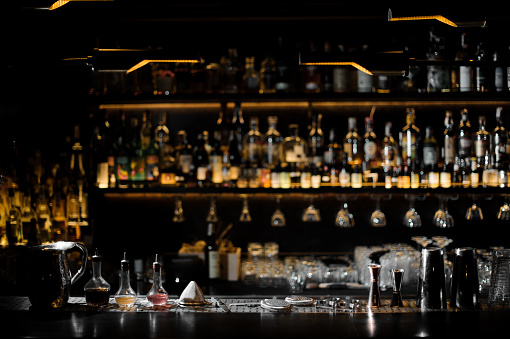 Blurred background of dark bar with bottles of alcohol and with barman essentials in the foreground