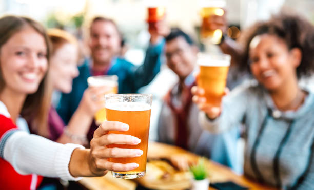 Blurred background of friends drinking and toasting beer at brewery bar restaurant patio - Happy hour promotion concept with people having fun together at brew out door pub - Focus on lower pint glass stock photo
