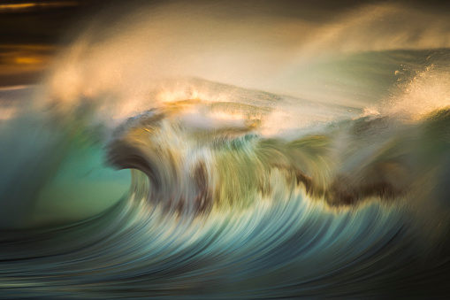Blurred motion of blue ocean wave crashing in golden light