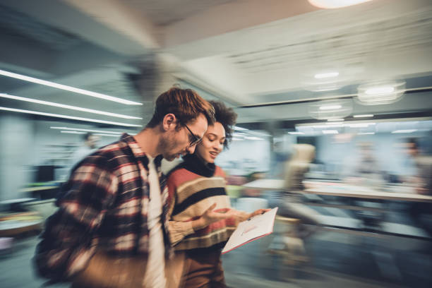 Blurred motion of young entrepreneurs reading reports in the office. Young business couple analyzing business documents while walking in a busy office. Blurred motion. busy office stock pictures, royalty-free photos & images