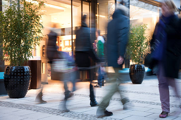 blurred people walking past illuminated fashion store - etalages kijken stockfoto's en -beelden