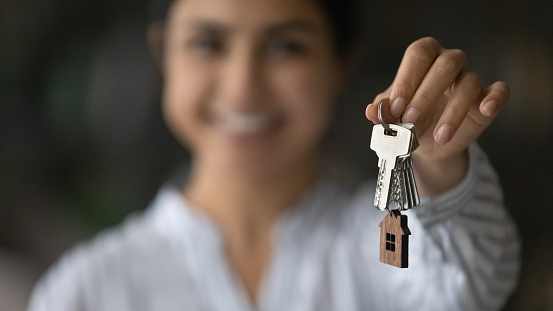 New home. Blurred portrait of smiling young female seller Real Estate Agent broker holding key in hand giving you client customer buyer renter after making successful deal. Soft focus on bunch of keys. Close up