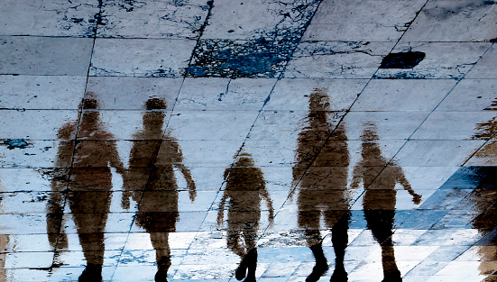 Blurry reflection shadow silhouette on wet city sidewalk of mysterious people walking away the night, low angle view