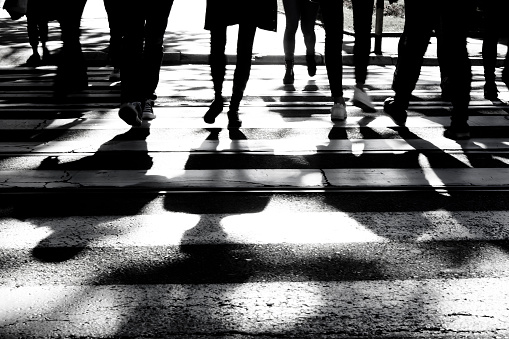 Blurry silhouettes and shadows of people crossing the street on crosswalk in black and white, only legs , unrecognizable