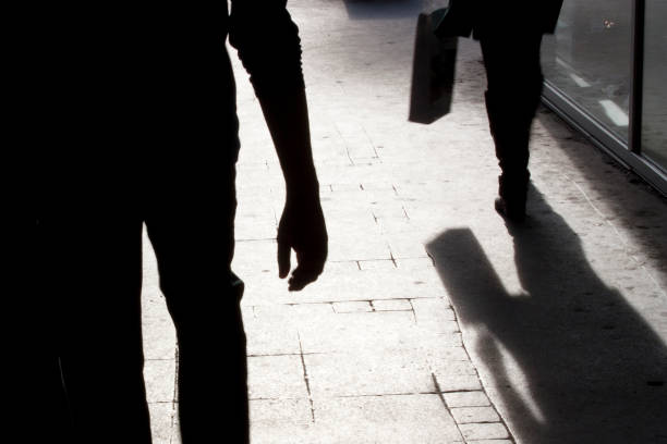 Blurry silhouette and shadows of two person walking Blurry silhouette and shadow of a woman carrying a bag and a man following her, in the city street in the night fear photos stock pictures, royalty-free photos & images