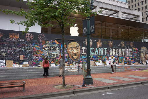 Portland, OR, USA - Jun 12, 2020: Passers-by stop and take a look at the boarded-up Apple Store in downtown Portland's Pioneer Place, which has become unofficial canvases for peaceful protest. Artists have also joined to promote peace over violence.