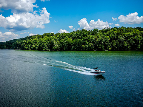 Speed boat on a lake with a trail of wake.  Green trees and white clouds in the sky.