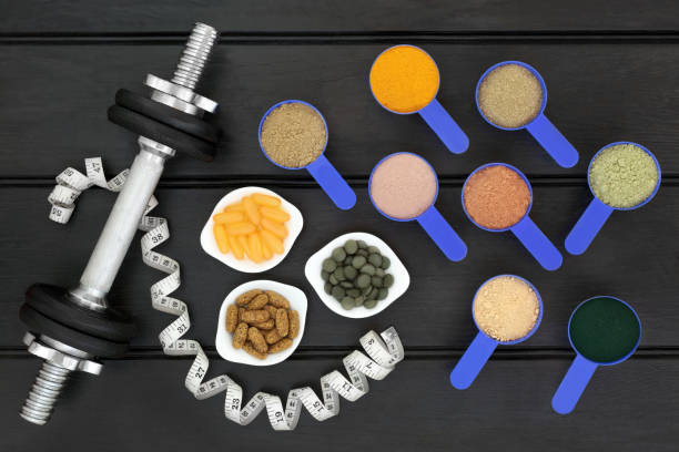 Body Building Food Supplement Powders and Dumbbells Body building dumbbell weights and tape measure with dietary food supplement powders,  multi vitamin and chlorella tablets with fish oil capsules. Top view on wood table. pea protein powder stock pictures, royalty-free photos & images