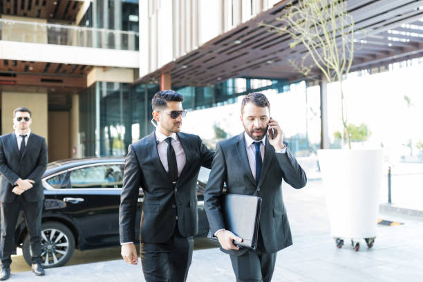 Bodyguard Ready To Provide Instant Protection Male employer using smartphone while protection specialist walking by him protection stock pictures, royalty-free photos & images