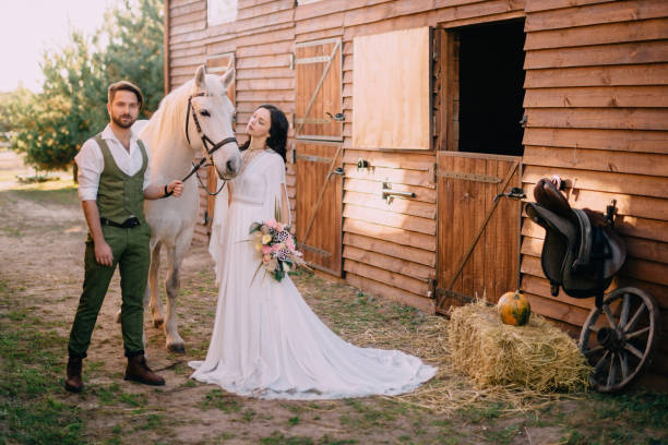 boho-style newlyweds standing near horse on ranch stock photo