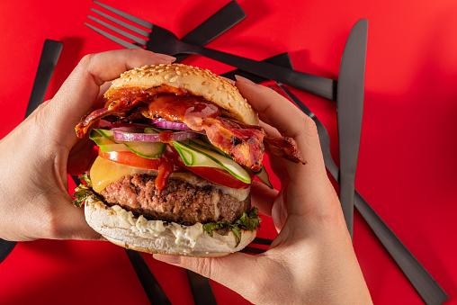 Bold fresh cheeseburger loaded with lettuce, cucumber, tomato, onion and bacon on vibrant red background