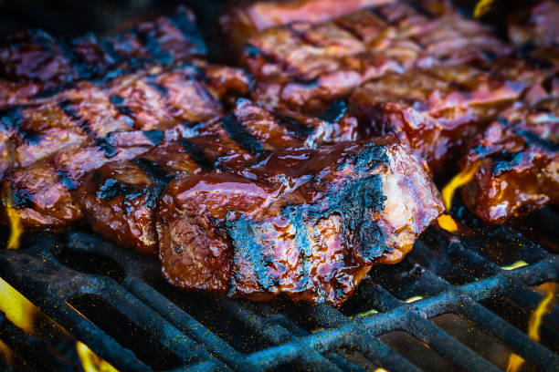 Boneless beef ribs grilling over flames BBQ boneless beef ribs grilling over flames with added barbecue sauce. Extreme shallow depth of field with blurred background with focus on front meat. Grilled Boneless Beef Short Ribs stock pictures, royalty-free photos & images