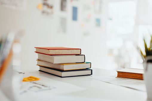 It's back to school time!  A large stack of textbooks to side makes frame composition.  The pile of objects lies on top of a wooden school desk with a green chalkboard in the background.  The blank blackboard in the background makes perfect copyspace!  Education background themes.