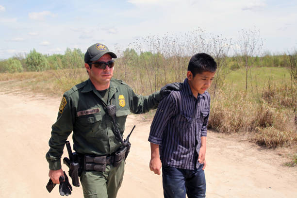 Border Patrol, Rio Grande Valley, Texas, Sept. 21, 2015 La Grulla, Texas, USA - September 21, 2015: A  Border Patrol agent takes a 14 year old Honduran boy into custody after apprehending him on the banks of the Rio Grande River attempting to enter the United States illegally.  There was a sharp increase in the number of unaccompanied Central American juveniles, most fleeing gang violence, trying to enter the U.S. illegally over the summer. border patrol stock pictures, royalty-free photos & images
