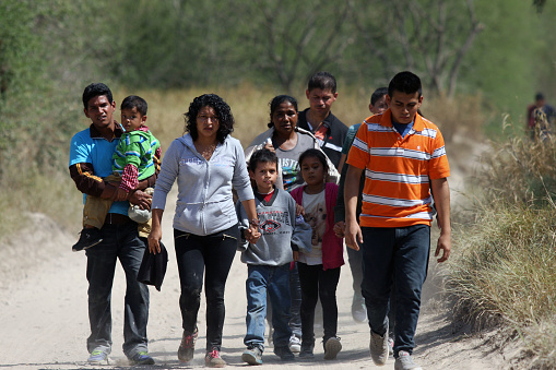 McAllen, Texas, USA - September 21, 2016: A group of Central Americans walks down a road prior to being picked up by the Border Patrol for illegally crossing the Rio Grande River into the U.S. in deep south Texas. There has been a flood of mothers with children and unaccompanied minors from Central America fleeing gang violence crossing illegally over the past several months.