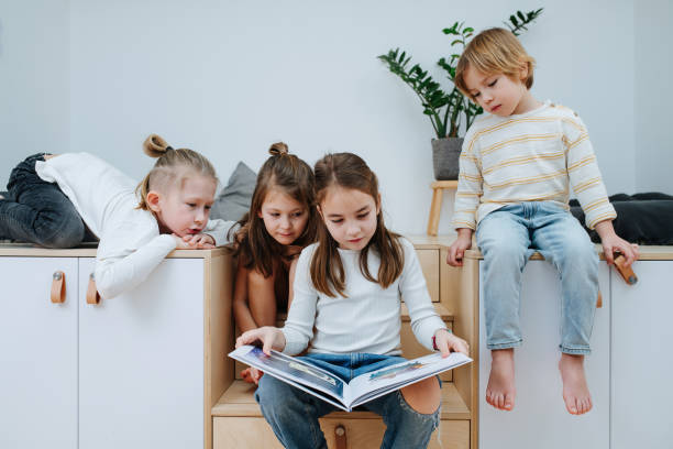 Bored children gathered in a room to read a picture book, all looking at it stock photo
