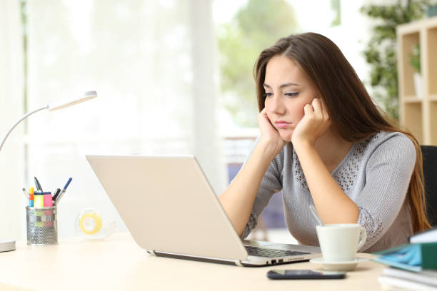 Bored entrepreneur looking at laptop screen at home Bored entrepreneur woman looking at laptop screen sitting on a desk at home boredom stock pictures, royalty-free photos & images