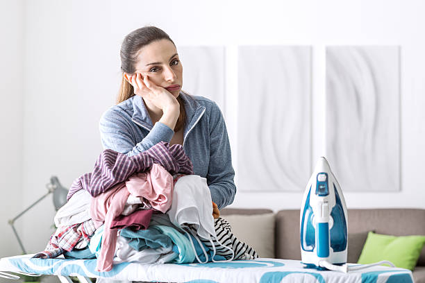 Boring household chores Disappointed unhappy housewife leaning on a pile of laundry on the ironing board housewife stock pictures, royalty-free photos & images