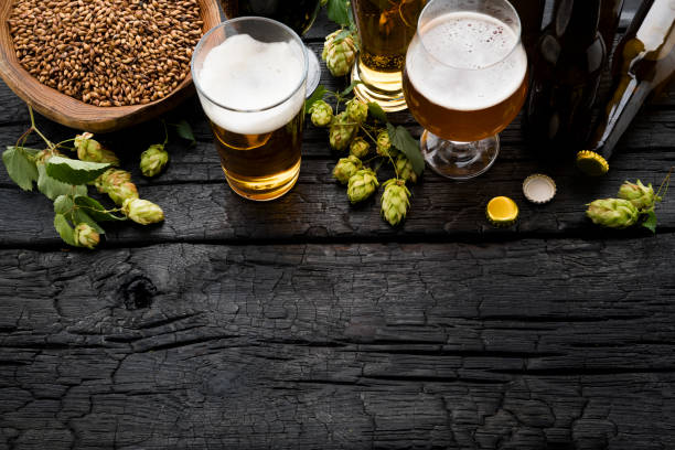 Bottle and Glass beer with Brewing ingredients. Beer and ingredients on black wooden table. Top View brewery stock pictures, royalty-free photos & images
