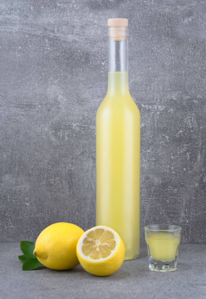 Bottle and shot of home made Limoncello Italian lemon liqueur and lemon fruits on grey surface. stock photo