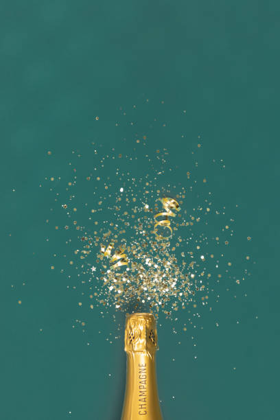 Bottle of champagne and confetti on green background, top view. stock photo