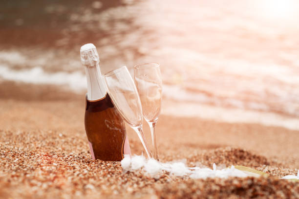 Bottle of champagne, two glasses and a diadem on the sand near the beach. stock photo