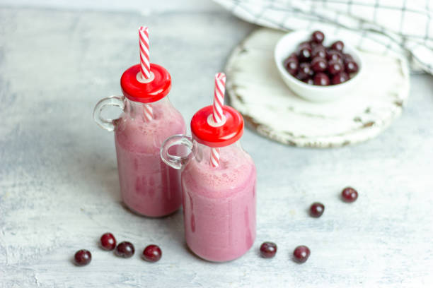 A bottle of cherry smoothies on a white background, cherries in bulk and in a plate. Morning summer breakfast stock photo
