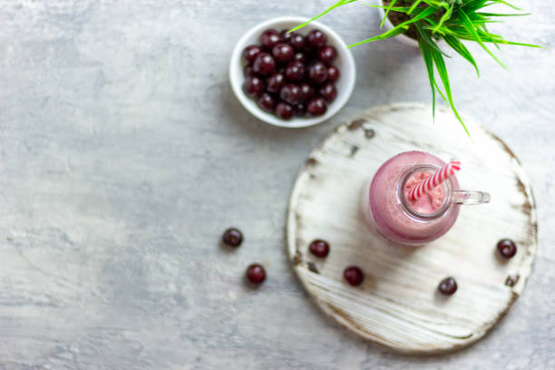 A bottle of cherry smoothies on a white background, cherries in bulk and in a plate. Morning summer breakfast stock photo