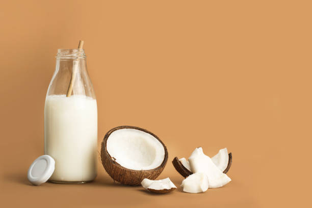 A bottle of coconut milk and pieces of coconut A bottle of coconut milk and pieces of coconut on a brown background coconut milk stock pictures, royalty-free photos & images