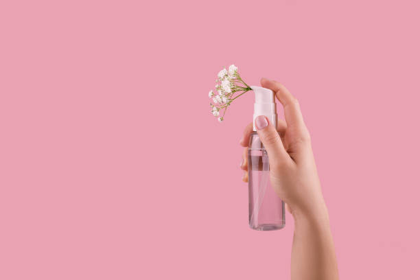bottle of perfume with spray scent of flowers woman hand holding bottle of perfume with spray scent of flowers on pink background. copy space deodorant stock pictures, royalty-free photos & images