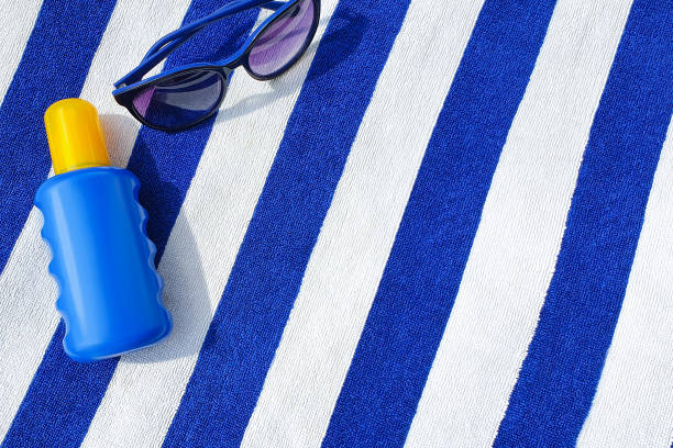 bottle of sunscreen and sunglasses on a striped beach towel. - beach towel imagens e fotografias de stock