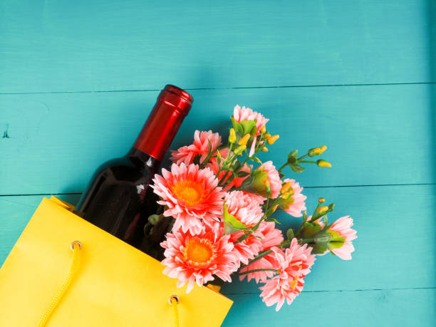 bottle of wine and flowers in the package on wooden background, space for text stock photo