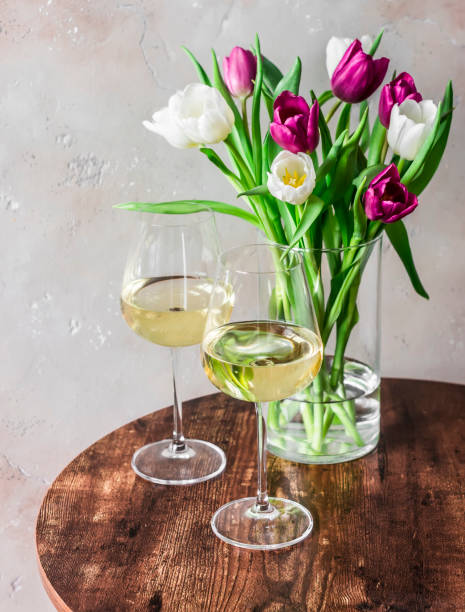 Bouquet of colorful tulips and two glasses of white wine on a wooden table stock photo