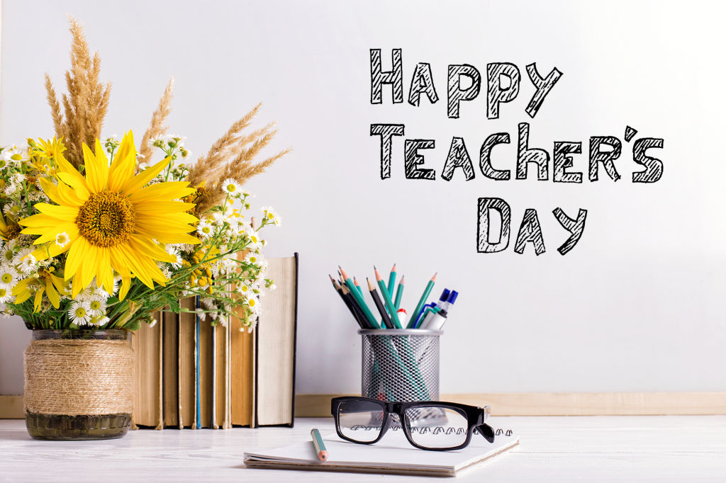 Bouquet of flowers, notebooks with eyeglasses on table. The inscription happy teacher's day..