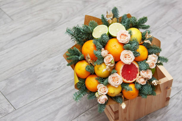 Bouquet of fruits and flowers. Orange, lemon, lime, tangerine, pink rose, spruce branches. Gray wooden background. stock photo