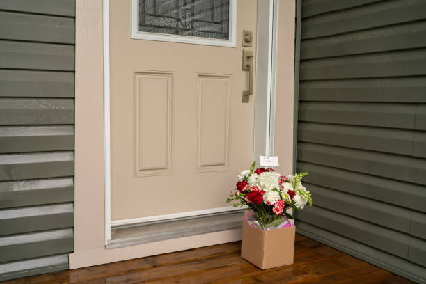 A bouquet of red white flowers in a carton box on a porch doorstep of a house. Surprise contactless delivery of flowers stock photo