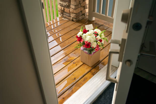 A bouquet of red white flowers in a carton box on a porch doorstep of a house. Surprise contactless delivery of flowers stock photo