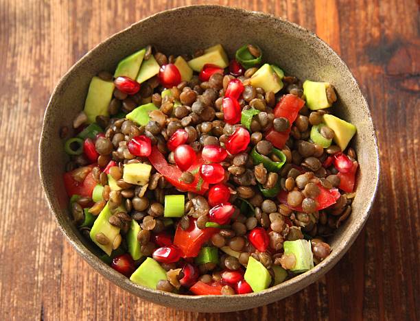 Bowl of brown lentil salad sitting on a wooden table top stock photo